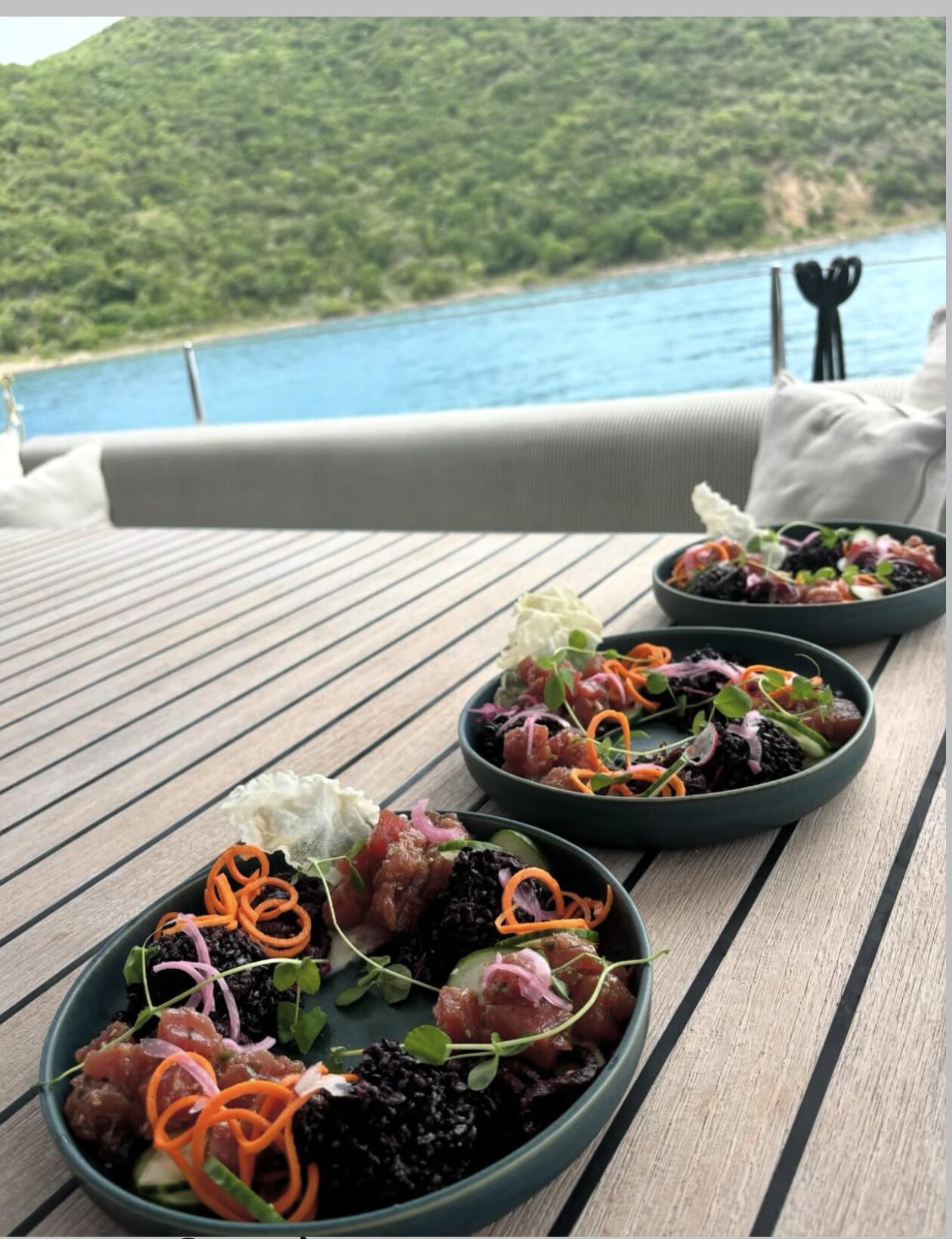 Three plates of tuna poke on a yacht table above a turquoise bay