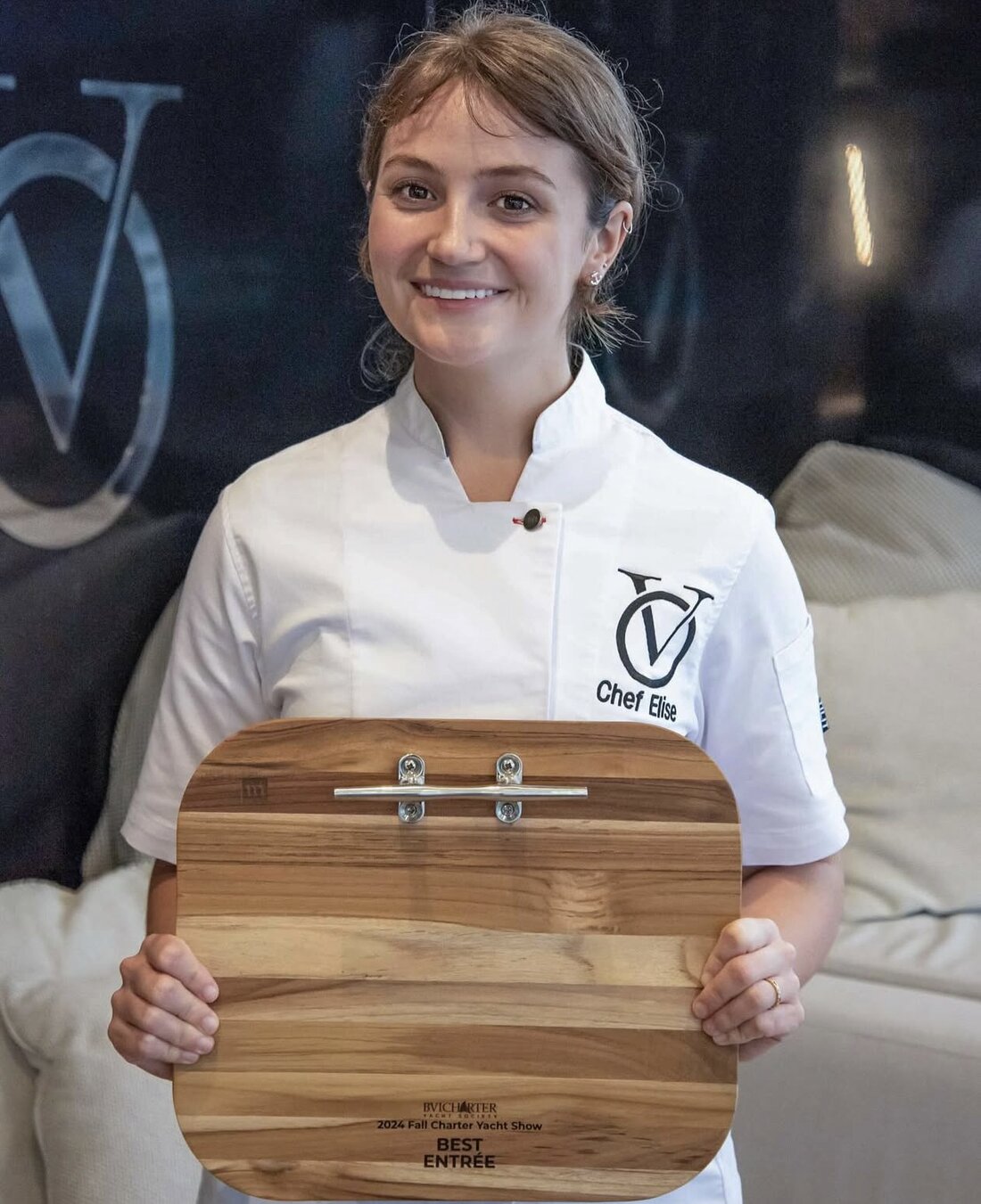Chef Elise Carvel in chef whites, holding her Best Entree award board